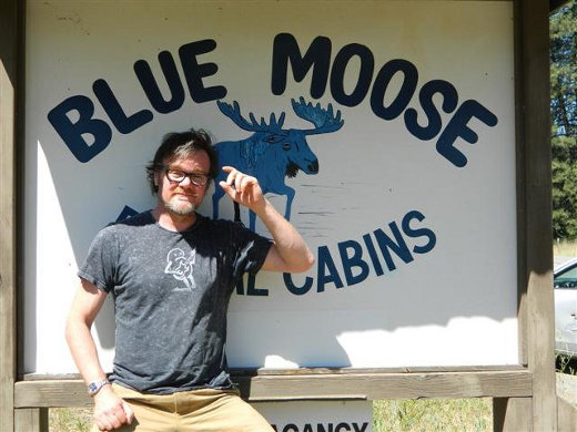 Bluemoose author Adrian Barnes posing in front of a Blue Moose sign in America.