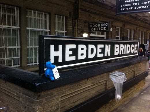 A (toy) blue moose sitting in front of the 'Hebden Bridge' sign at the town's station.
